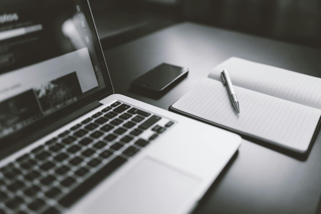 A sleek black and white workspace featuring a laptop, smartphone, and notebook with a pen, highlighting modern technology.
