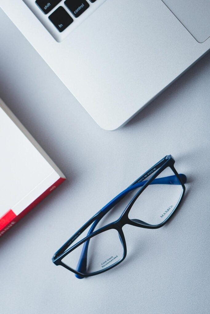 Close-up of blue eyeglasses on a gray desk with a laptop, ideal for productivity themes.